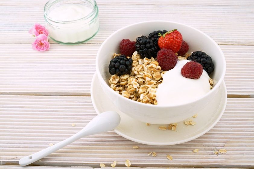 A wooden bowl of yogurt, berries, oats and seeds on a linen cloth